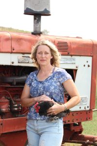 woman holding black chicken with tractor behind her